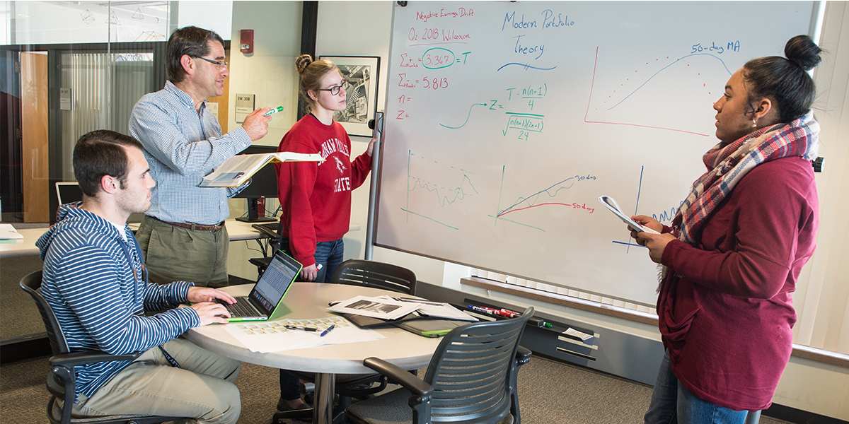 Three  students and a professor looking at a whiteboard